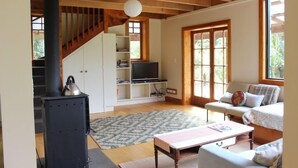 Una sala de estar acogedora con chimenea, un sofá, un televisor y una escalera que sube a un altillo.