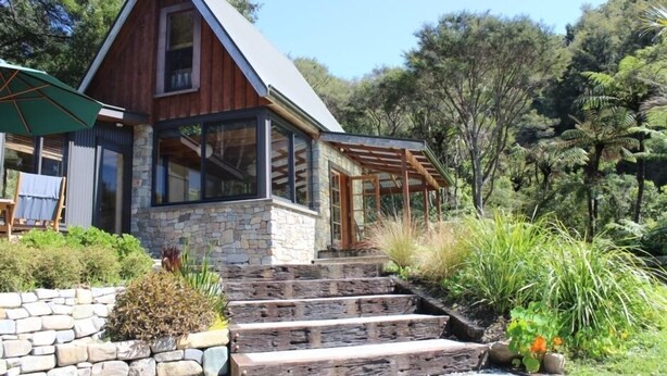Una casa moderna con base de piedra, revestimiento de madera y ventanas grandes.