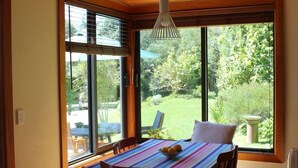 Un comedor con una mesa lista para dos, ventanas amplias con persianas y un colgador de luz.