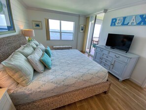 Een slaapkamer met een groot bed, een televisie, een raam met uitzicht op zee, en een bordje met de tekst 'RELAX' aan de muur.