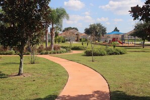 Explore the playground surrounded by lush greenery and mature trees, with a curved pathway leading to a fun play area.