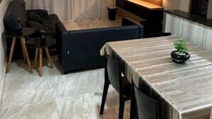 Un salon comprenant un canapé, un téléviseur fixé au mur, un ventilateur de plafond et un coin repas avec une table et des chaises.