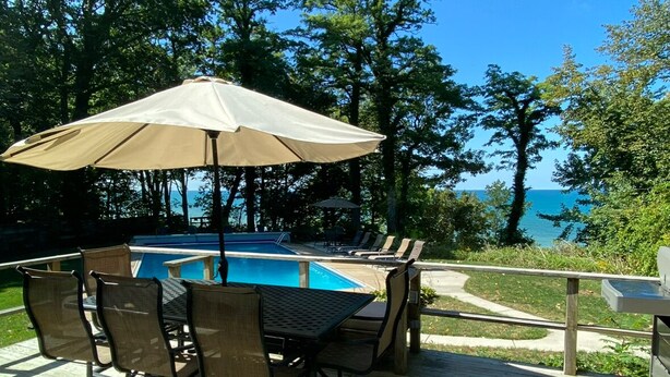 A poolside deck with a table and chairs, a large umbrella, and a view of the ocean. - Spa House:On Lake Michigan w/ Pool, Hot Tub, Sauna (Benton Harbor)