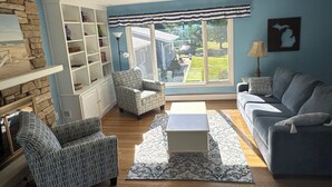 A living room with a stone wall, a large window, a blue sofa, a white coffee table, and a patterned rug. - Spa House:On Lake Michigan w/ Pool, Hot Tub, Sauna (Benton Harbor)
