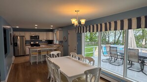 A modern kitchen with white cabinets, a stainless steel refrigerator, and a dining area with a white table and chairs. - Spa House:On Lake Michigan w/ Pool, Hot Tub, Sauna (Benton Harbor)