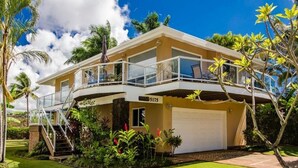 A two-story house with a balcony, a garage, and a well-maintained garden with tropical plants.