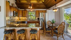 A kitchen with wooden cabinets, a granite countertop, a stainless steel refrigerator, and a dining area with wicker chairs and a table.
