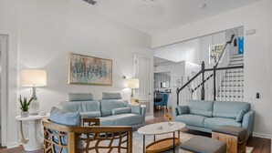 A spacious living room with a light blue sofa set, a wooden coffee table, and a modern chandelier. - Luxury 5 Stars Home w/Princess & Mickey Themed Rooms, Game Room Private Pool/Spa (Kissimmee)