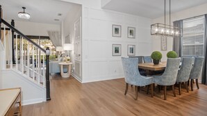 A modern dining area with a wooden table, grey upholstered chairs, and a chandelier. - Luxury 5 Stars Home w/Princess & Mickey Themed Rooms, Game Room Private Pool/Spa (Kissimmee)