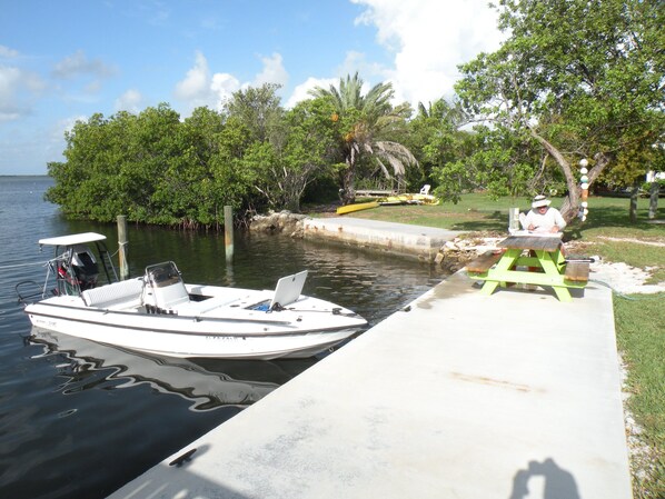 A boat docked at a pier with a picnic table and a person sitting at the table. - Cottage with swimming pool and dockage, just minutes to Key West! (Cudjoe Key)
