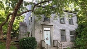 Une maison à deux étages avec une porte d’entrée bleu clair, un petit porche et un escalier en pierre menant à l’entrée.
