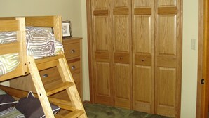 Una cama litera con escalera de madera, un aparador y un armario de madera con varias puertas.