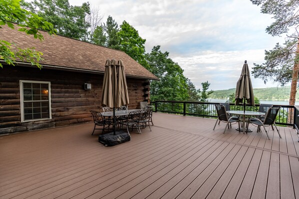 A wooden deck with a table and chairs, two umbrellas, and a view of a lake.