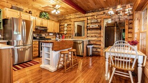 A wooden cabin kitchen with a refrigerator, stove, sink, and wooden dining table with chairs.