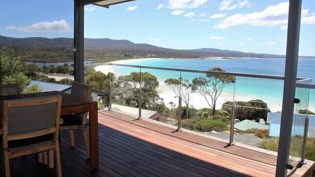 A wooden deck with a glass balustrade overlooking a beach and ocean. - SEA EAGLE COTTAGE Bay of Fires PEOPLES CHOICE TAS (Binalong Bay)