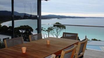 A wooden table with chairs, a glass balustrade, and a view of a coastal landscape.