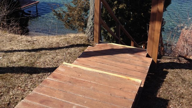 A wooden staircase leading to a gazebo by a lake with clear blue water and distant hills.