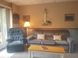 Ein Wohnzimmer mit grauem Sofa, blauem Sessel, Couchtisch aus Holz und einer Lampe.