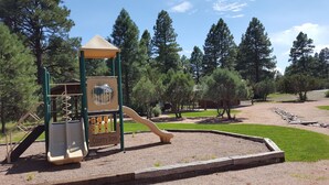 A playground with a slide and climbing structures, surrounded by trees and a gravel path. - Beautiful Bison Ridge Cabin that has it all... (Show Low)