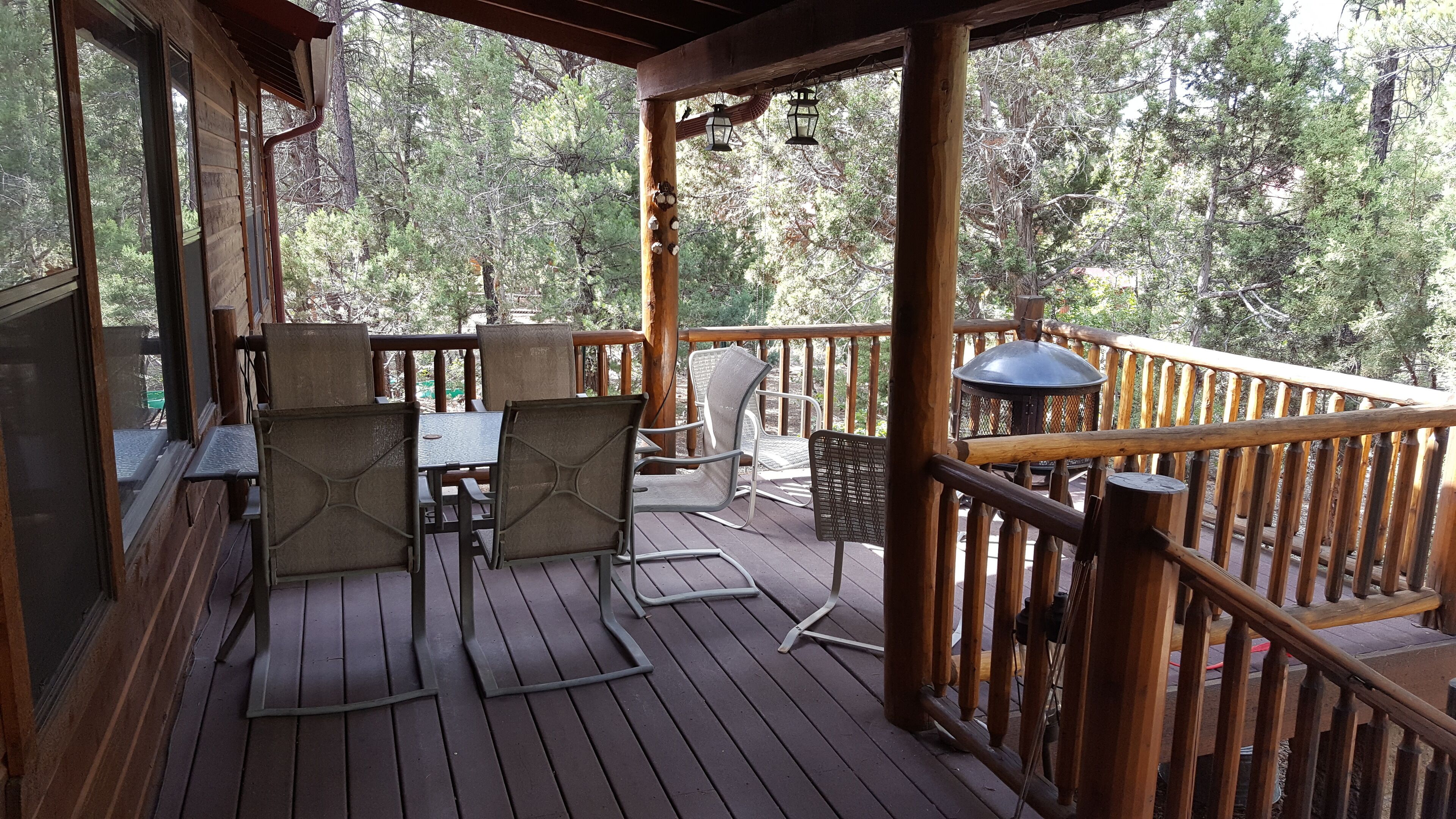 A wooden deck with outdoor furniture, including chairs and a table, overlooking a forested area.