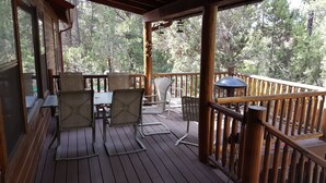 A wooden deck with outdoor furniture, including chairs and a table, overlooking a forested area. - Beautiful Bison Ridge Cabin that has it all... (Show Low)