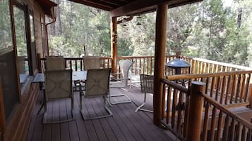 A wooden deck with outdoor furniture, including chairs and a table, overlooking a forested area.