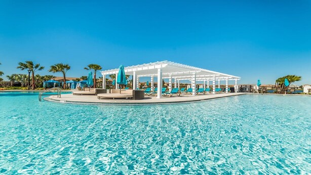 Ein Resort-Pool mit weißer Pergola, Liegestühlen und Palmen.