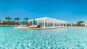 Piscina de un resort con una pérgola blanca, sillas de descanso y palmeras.