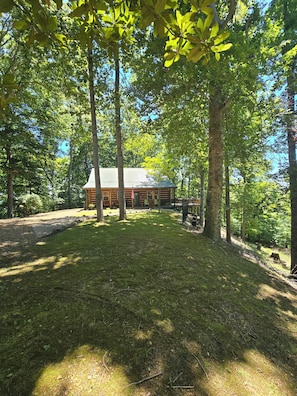 A cabin with a metal roof, surrounded by trees and a grassy area. - Lake Cumberland custom log cabin home on 32 wooded acres (Nancy)