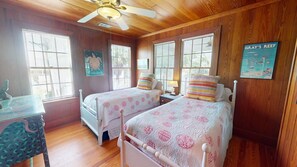 A bedroom with two beds, wooden walls, and a ceiling fan.