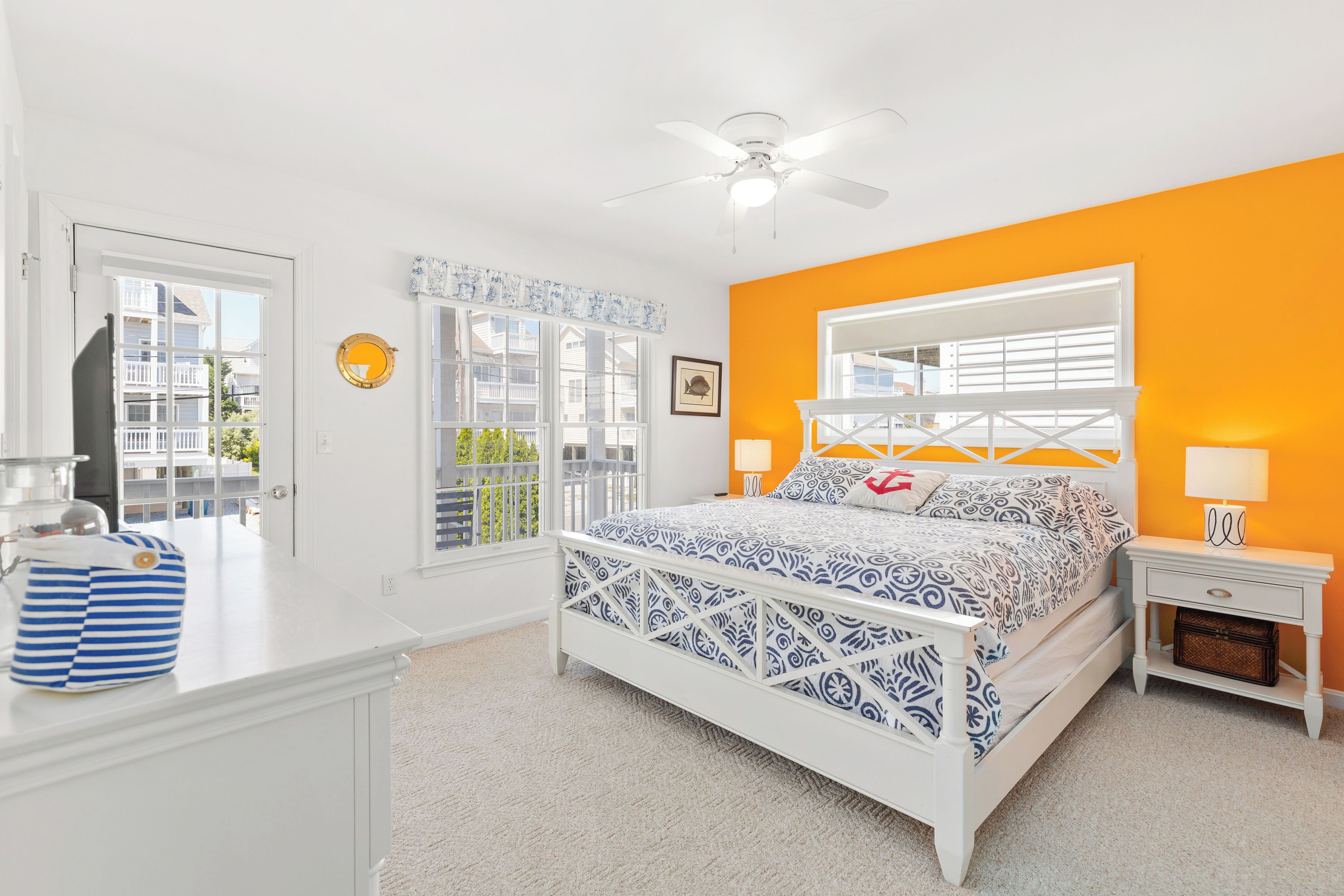 A bedroom with a bed, a nightstand, a dresser, a ceiling fan, and a window with a view of buildings.