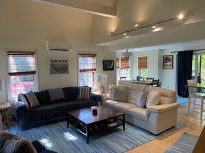 A living room with a dark-colored sofa, a light-colored sofa, a wooden coffee table, and a dining area with a table and chairs.