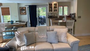 Een woonkamer met een beige bank, een eethoek met een tafel en stoelen, en een keuken met kastjes en apparatuur.