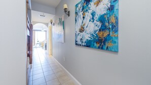 Een gang met een betegelde vloer, een groot abstract schilderij aan de rechtermuur en een deur aan het einde die naar een andere kamer leidt.