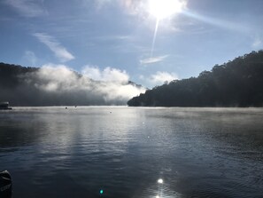Un lago tranquilo con un bote en primer plano y una colina boscosa al fondo.