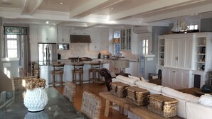 Un'ampia cucina con mobili bianchi, una cucina centrale con sgabelli da bar e un'area pranzo con tavolo in vetro e cesti di vimini.