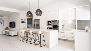 Een moderne keuken met witte kasten, roestvrijstalen apparatuur en een centraal eiland met barkrukken.