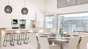 Een moderne keuken met witte kasten, roestvrijstalen apparatuur en een groot kookeiland met barkrukken.
