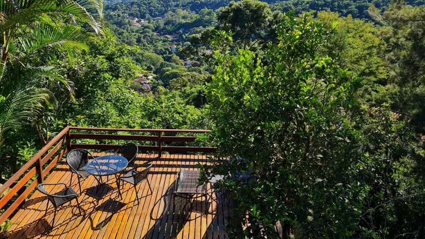 A wooden deck with outdoor seating, surrounded by lush greenery and mountains in the background. - Cozy house, beautiful view, ideal for families and couples. OI FIBER INTERNET. (Petropolis)