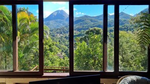 A room with large windows offering a view of a mountainous landscape with lush greenery. - Cozy house, beautiful view, ideal for families and couples. OI FIBER INTERNET. (Petropolis)
