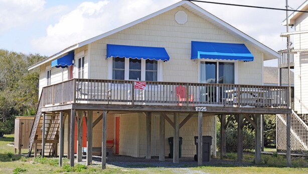 A two-story building with a balcony, a visible garage door, and a sign indicating a vacation rental. - Fun-N-The Sun - 2 BR Home; Dog Friendly with an Ocean View! (Surf City)