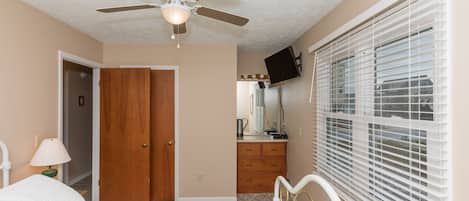 A bedroom with a bed, a ceiling fan, a dresser, a mirror, and a window with blinds.