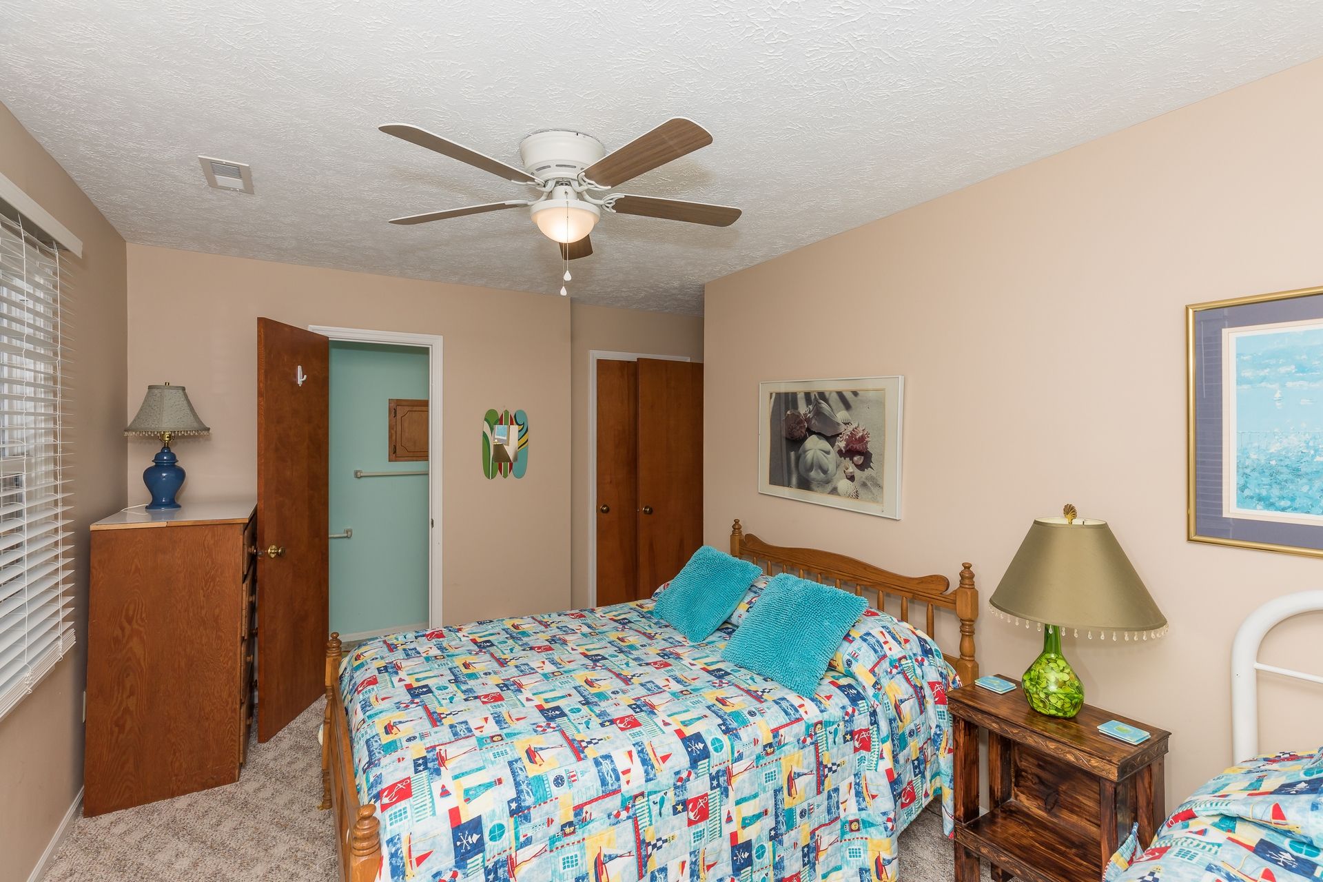 A bedroom with a bed, a nightstand, a ceiling fan, a door, and a window with blinds.