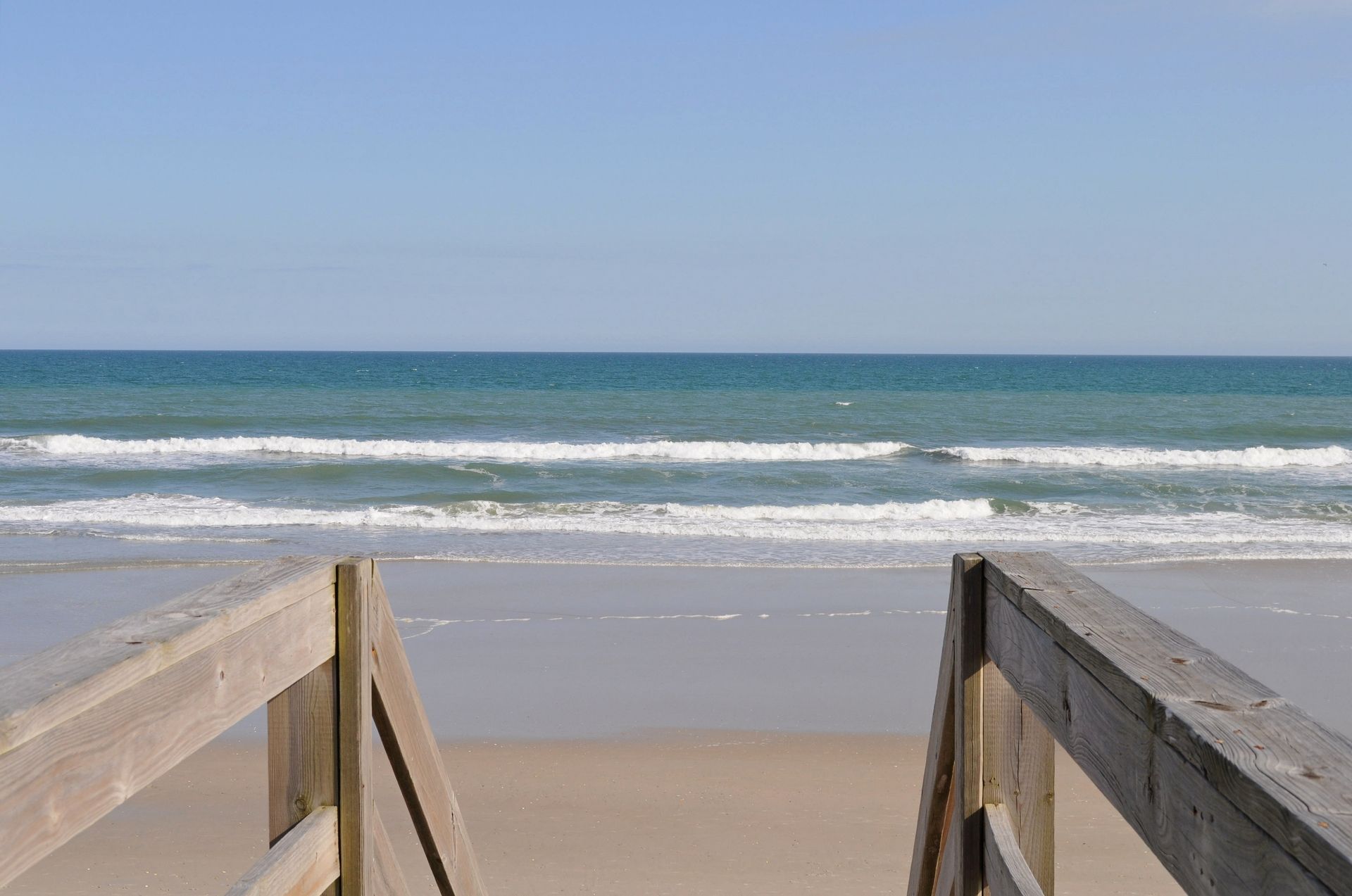 Una passerella in legno conduce a una spiaggia sabbiosa con onde nell'oceano.