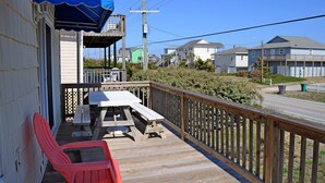 A wooden deck with picnic tables and chairs, overlooking a residential area with houses and a road. - Fun-N-The Sun - 2 BR Home; Dog Friendly with an Ocean View! (Surf City)