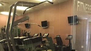 Une salle de sport équipée de matériel d’exercice, dotée d’un mur recouvert de miroirs et d’un ventilateur au plafond.