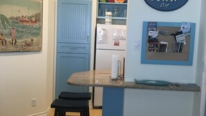 Une cuisine avec une porte bleue, un réfrigérateur et un mur orné d’une affiche sur laquelle on peut lire : « GARDONS NOTRE CALME ET ALLONS SURFER ».