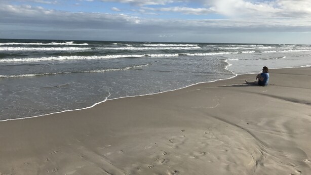 Une plage avec des vagues et une personne assise sur le sable.