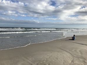 Ein Strand mit Wellen und einer Person, die im Sand sitzt.