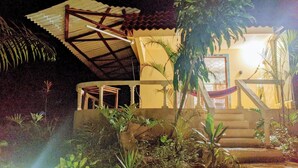 A building with a staircase leading to a porch, surrounded by tropical plants.